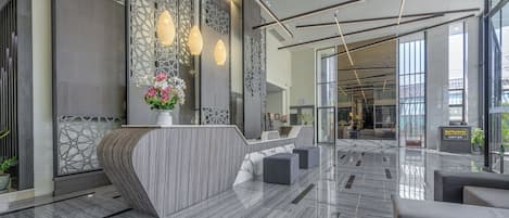 Un hall d’hôtel moderne avec un comptoir d’accueil, un espace salon et de grandes fenêtres.