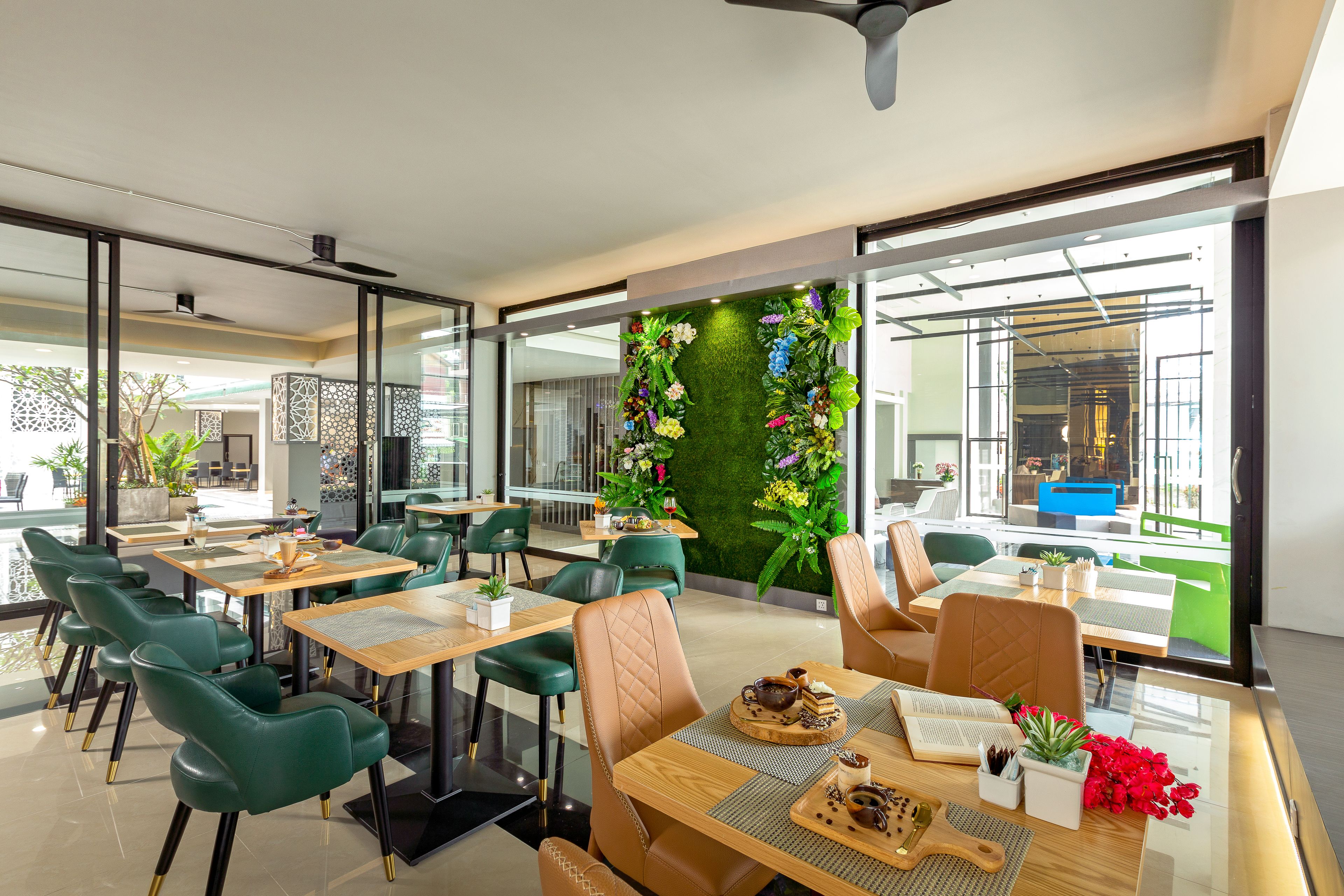 A modern dining area with green chairs, wooden tables, and a green wall with floral decorations.