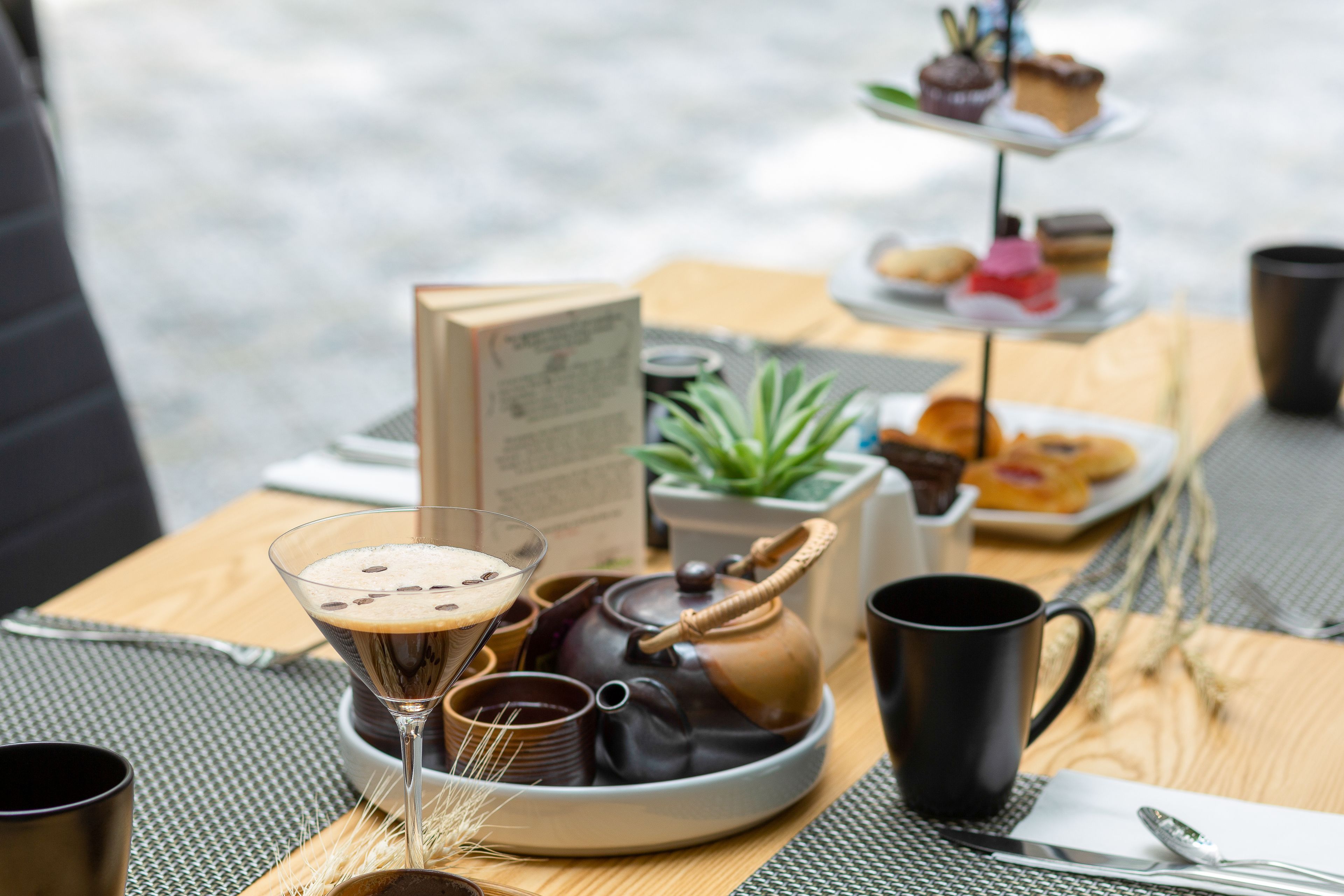 Een tafel met een theepot, een martini-glas, een menukaart en een etagère voor desserts.