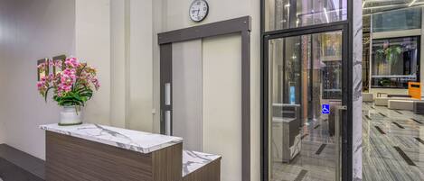 A reception area with a marble counter, a clock, and a glass door leading to a lobby with a patterned floor.