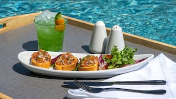 Una bandeja con una bebida verde, un plato de aperitivos y saleros y pimenteros junto a una piscina.