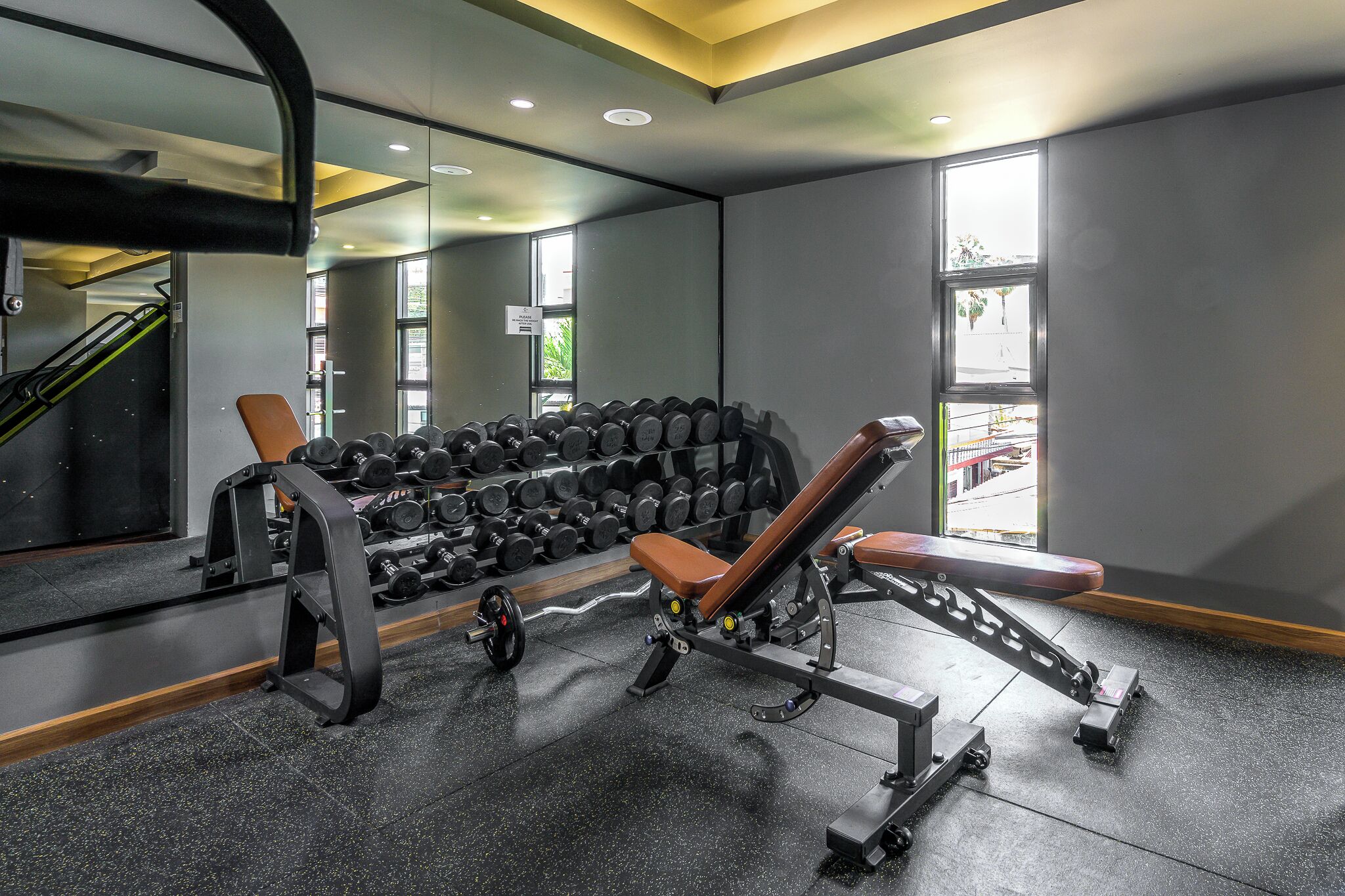 A gym with weightlifting equipment, a bench, and a rack of dumbbells.