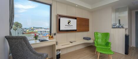 A modern hotel room with a large window, a mounted TV, a desk, and two chairs.