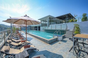 Un área de piscina en la azotea con sillas de descanso, una estructura de cristal y vistas despejadas del paisaje circundante.
