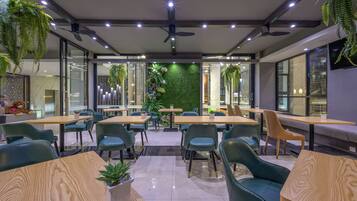 Un comedor moderno con mesas y sillas, ventiladores de techo y plantas verdes.