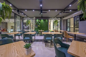 Un comedor moderno con mesas y sillas, ventiladores de techo y plantas verdes.