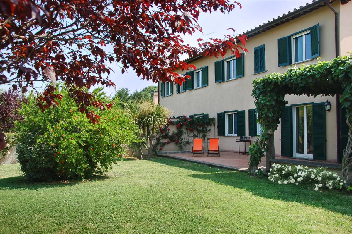 A two-story building with a garden, outdoor seating, and a pergola.