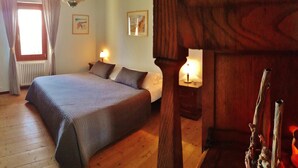 A bedroom with a large bed, two bedside lamps, a radiator, and a wooden wall. - Cà Gennara B&B (Alto Reno Terme)