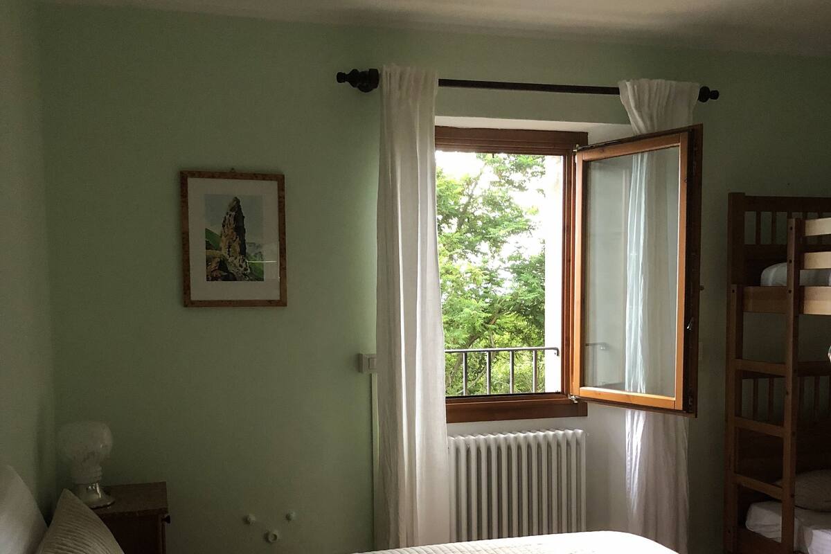 Una camera da letto con un letto, una finestra con tende, un termosifone e una mensola in legno.