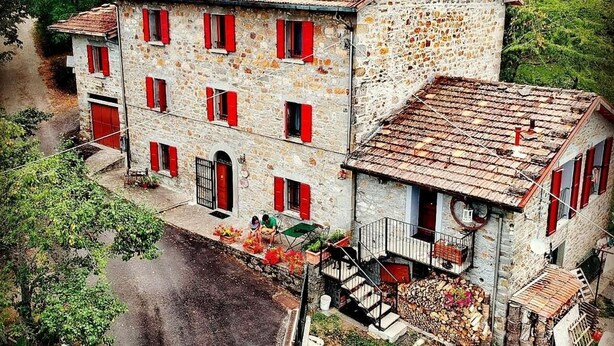 A stone building with red shutters, a staircase, and a garden area with plants and flowers. - Cà Gennara B&B (Alto Reno Terme)