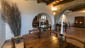 A dining area with a wooden table, chairs, and a candle centerpiece. There are stone arches and wooden beams on the ceiling.