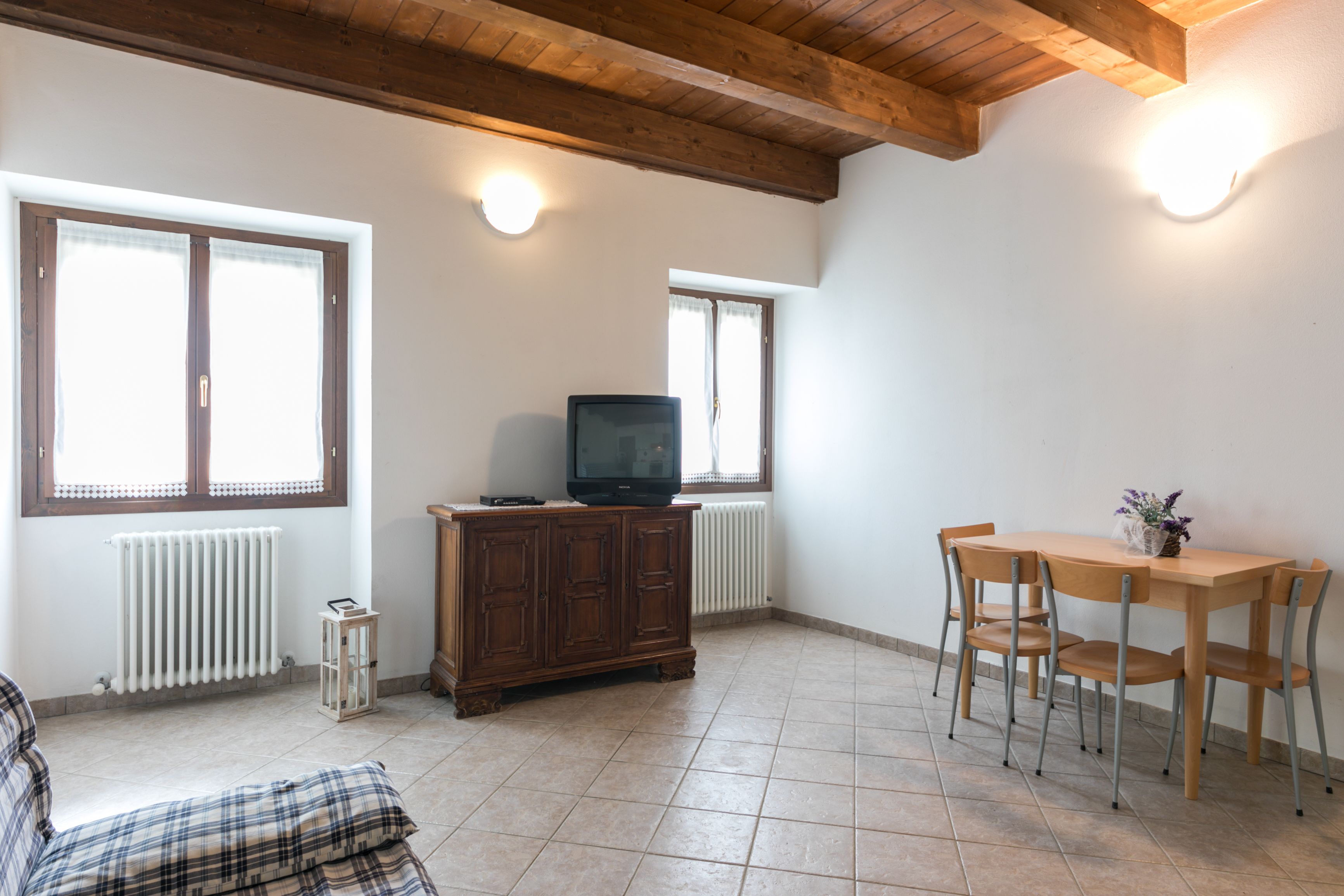 Una habitación con techo de madera, un televisor sobre un mueble, una mesa de comedor con sillas y un radiador.