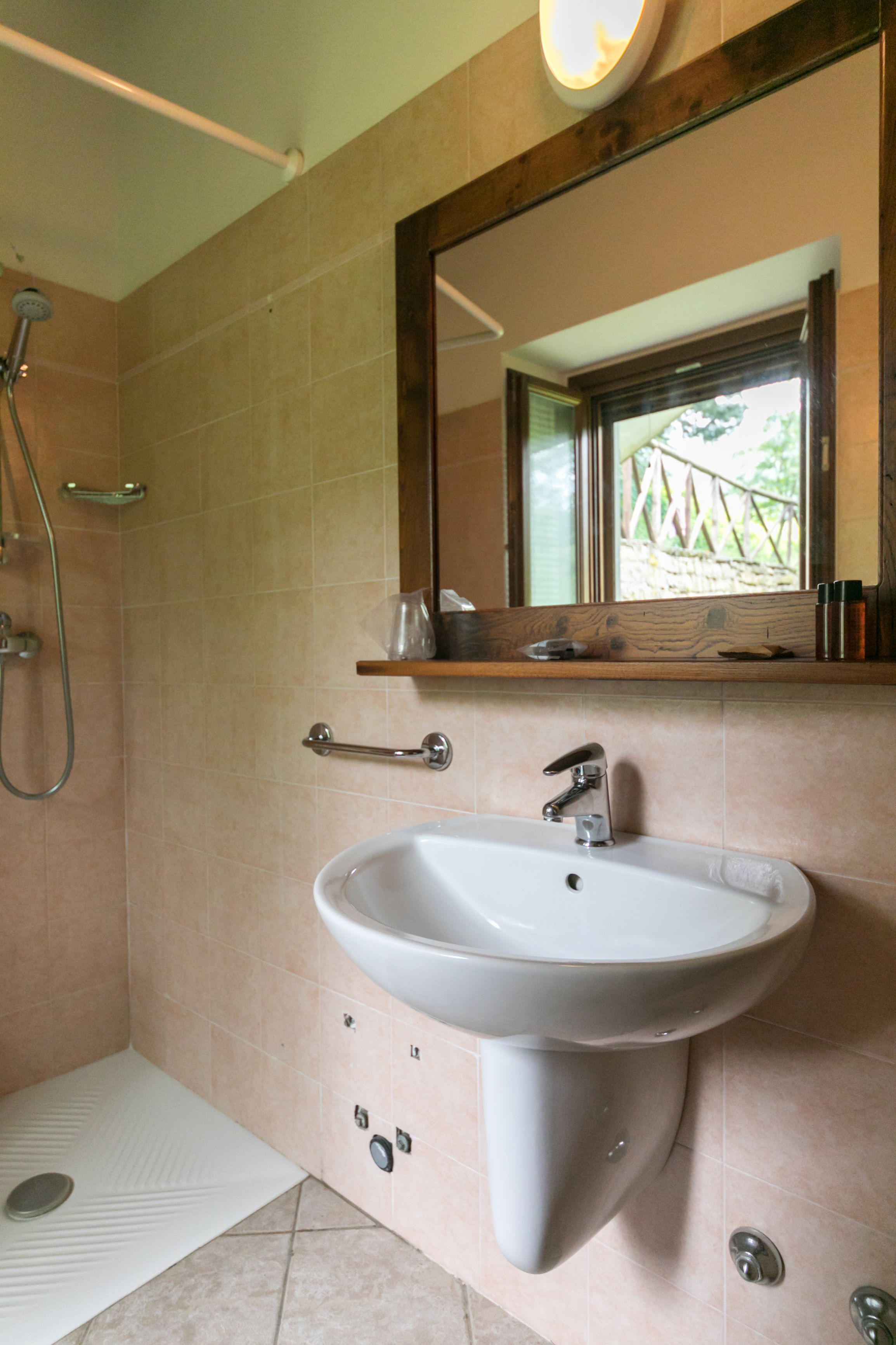 A bathroom with a sink, mirror, shower, and a window with a view of greenery.