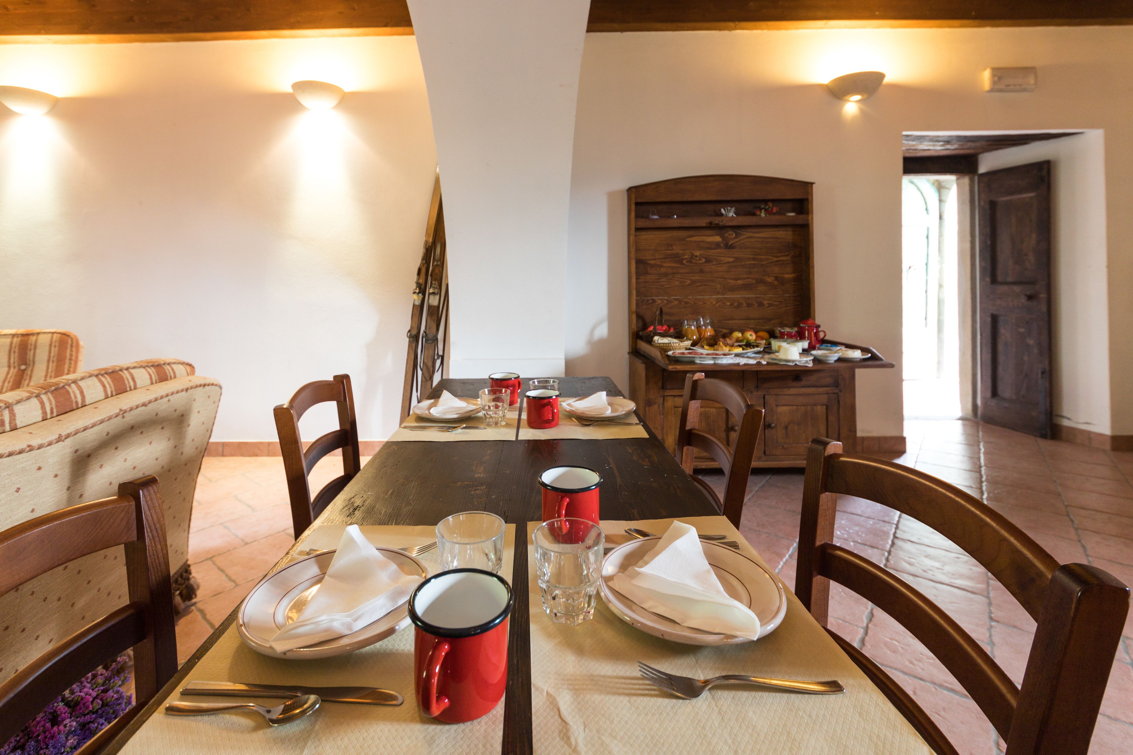 Ein Essbereich mit einem langen Tisch, gedeckt für vier Personen, Holzstühle und eine Holzkommode im Hintergrund.