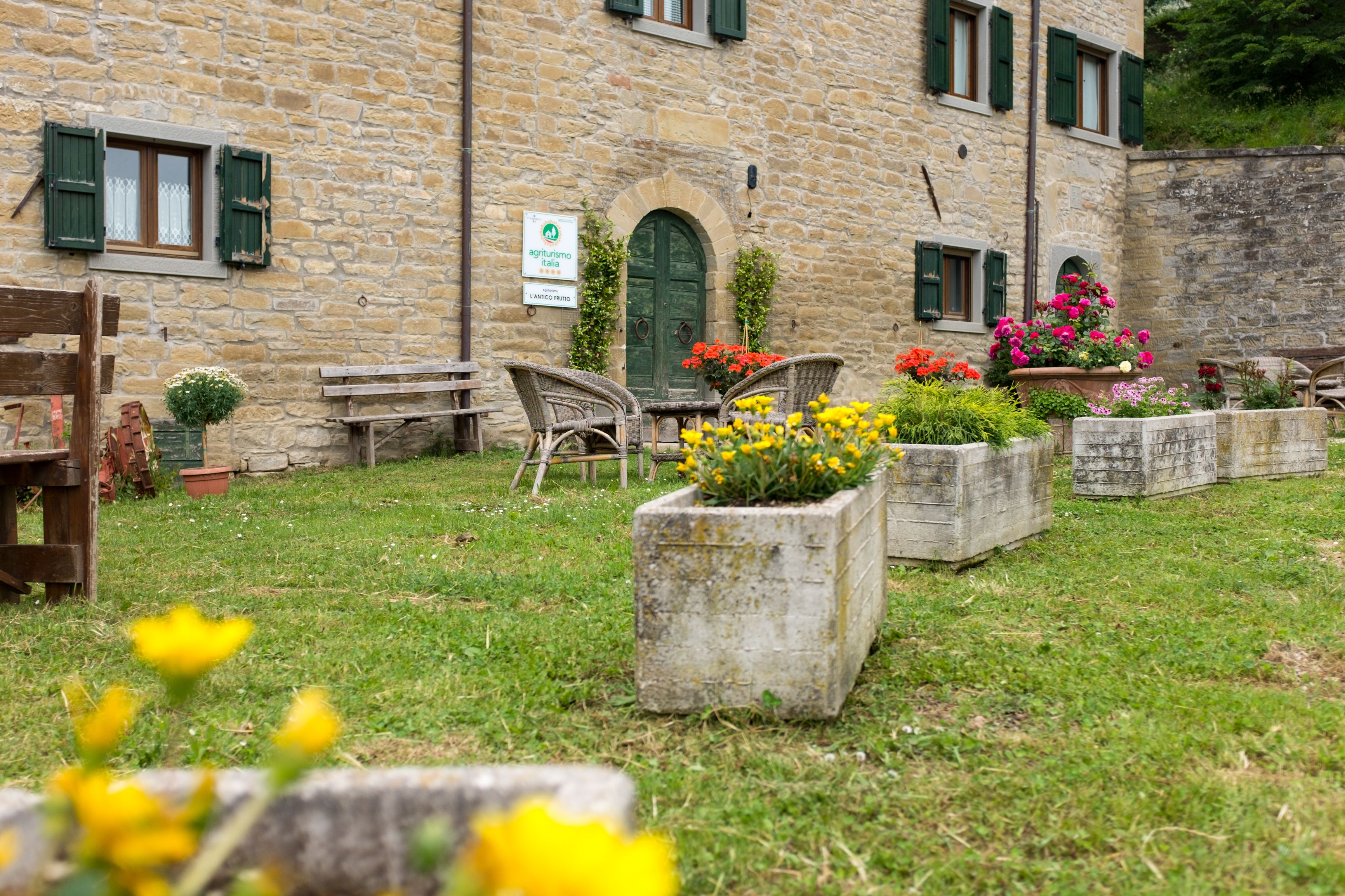 A stone building with a green door and windows, outdoor seating, and flower planters.