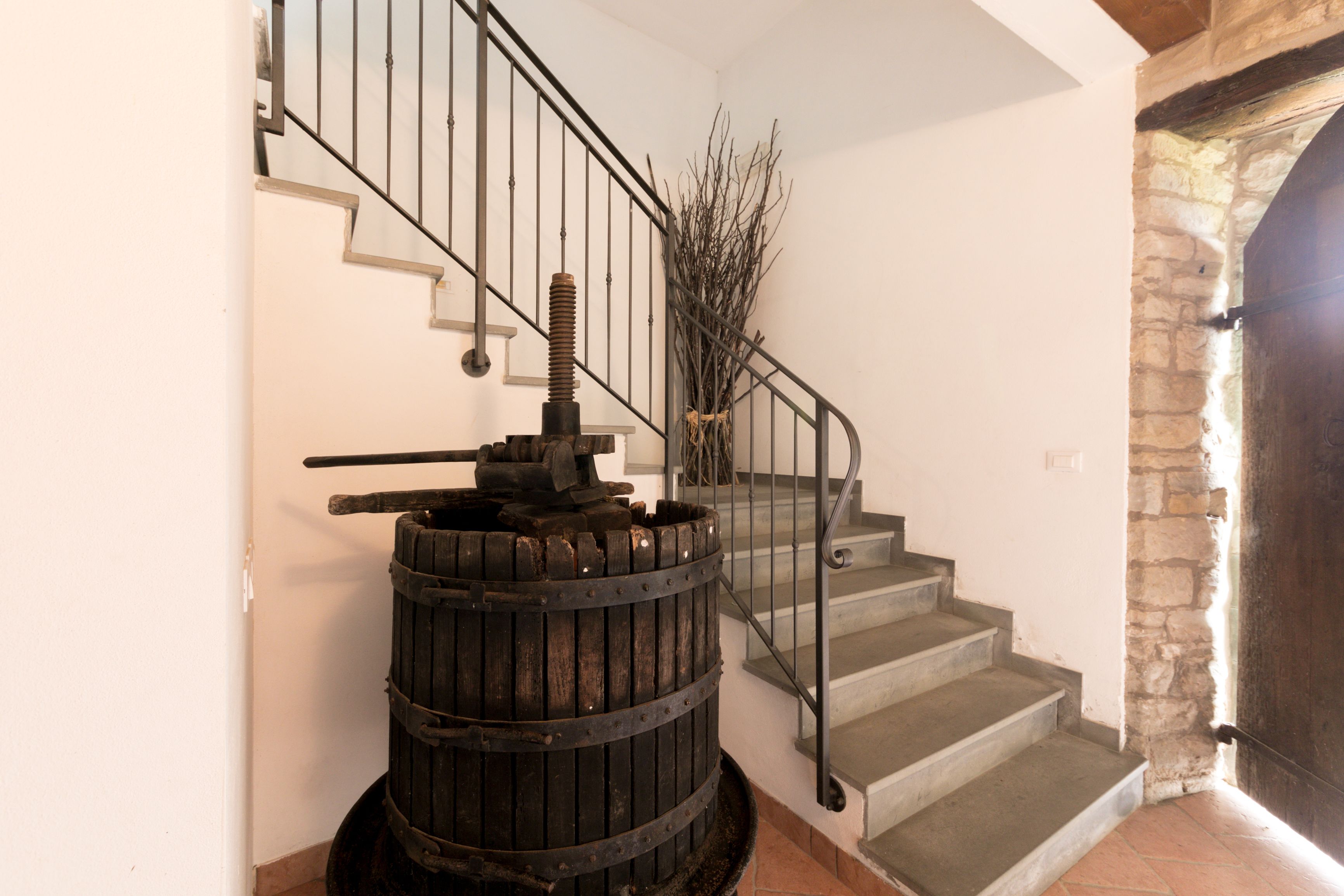 Un escalier avec une rampe en métal, un tonneau en bois et un mur de pierre.
