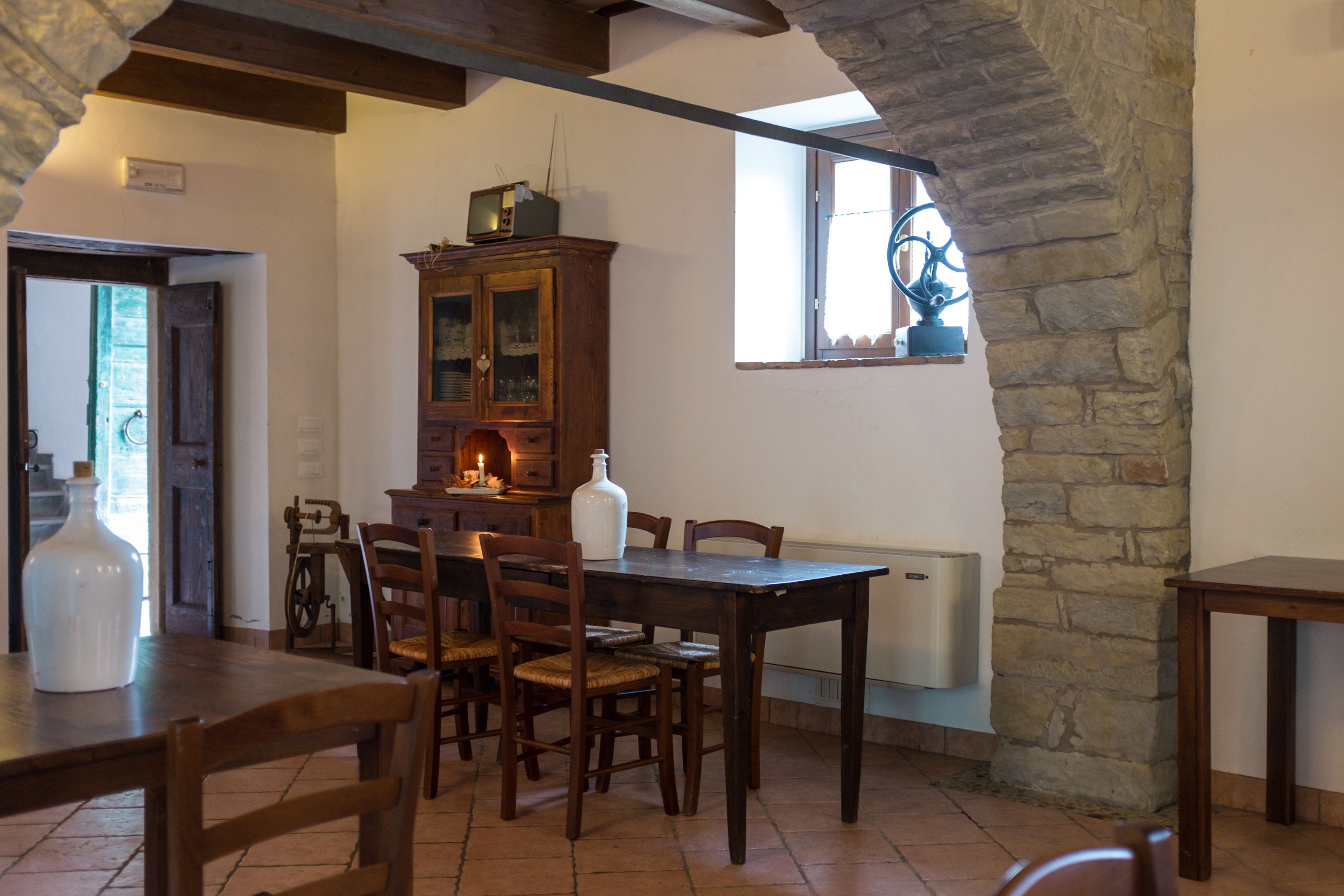 Un coin repas avec une table et des chaises en bois, un meuble contenant un téléviseur et un mur en pierre.