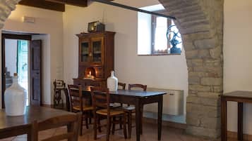 Un coin repas avec une table et des chaises en bois, un meuble contenant un téléviseur et un mur en pierre.
