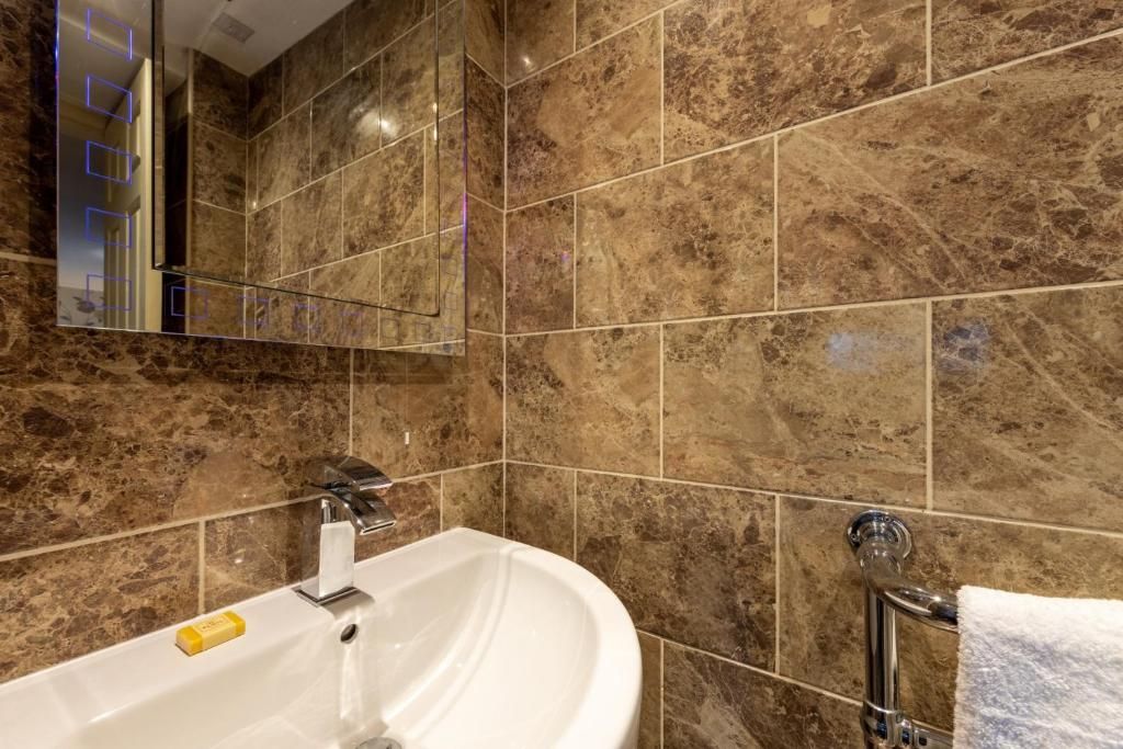 Un baño con un lavamanos blanco, un espejo y un perchero para toallas.