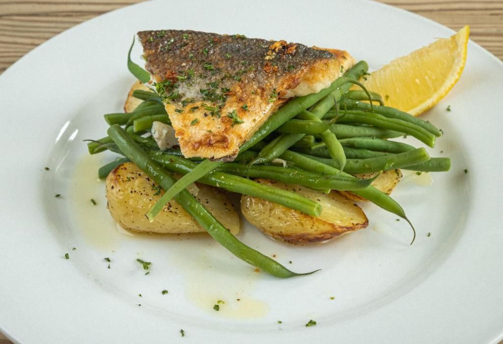 A plate with a piece of fish, green beans, and potatoes.