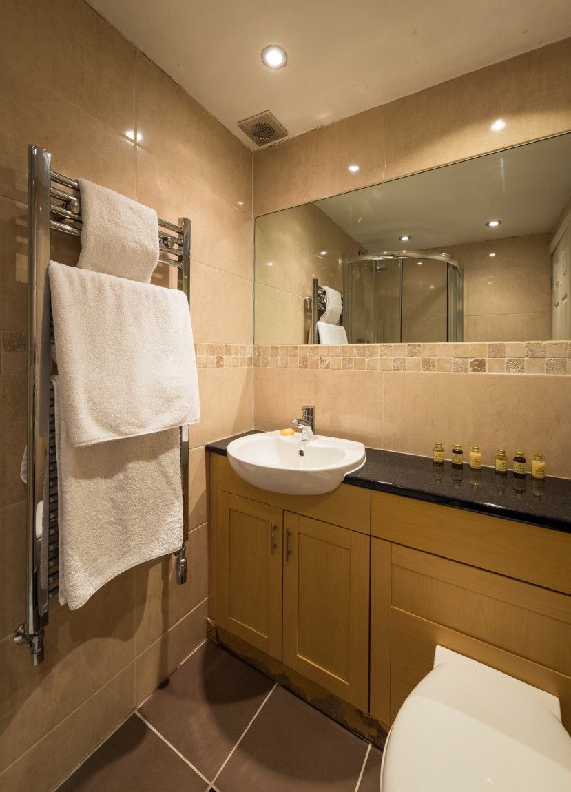 A modern bathroom with a beige tiled wall, a white sink, a mirror, and a towel rack with two towels.