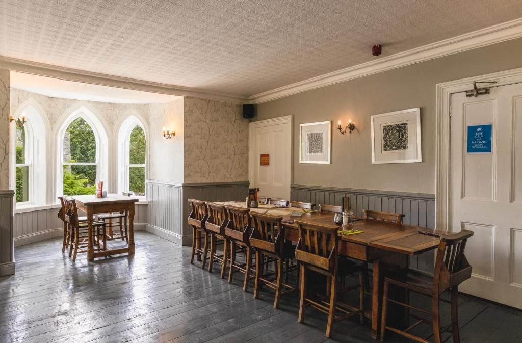 A dining area with a long wooden table and chairs, a window with a view of greenery, and a wall-mounted light fixture.