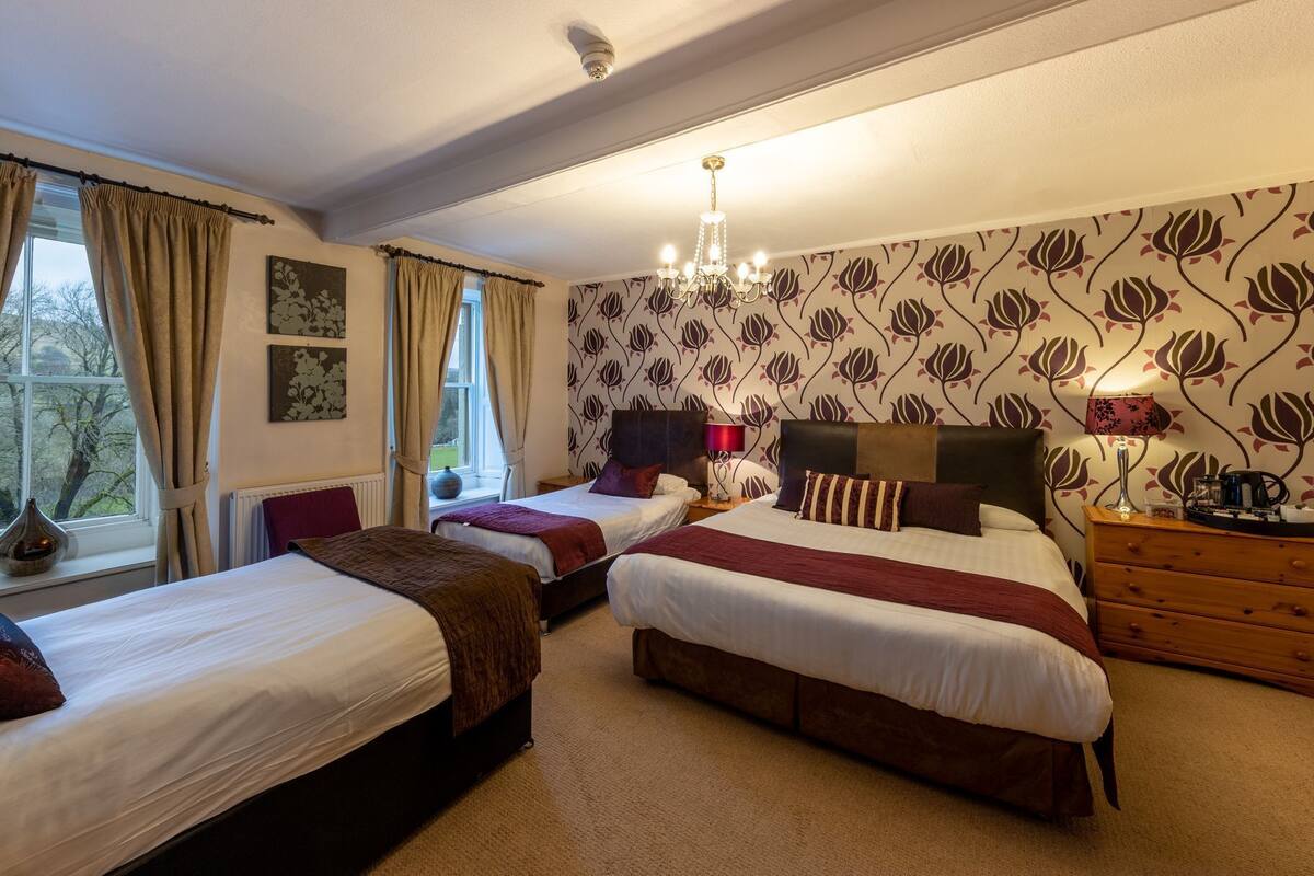 A hotel room with two single beds, a chandelier, a wooden dresser, and a floral wallpaper.