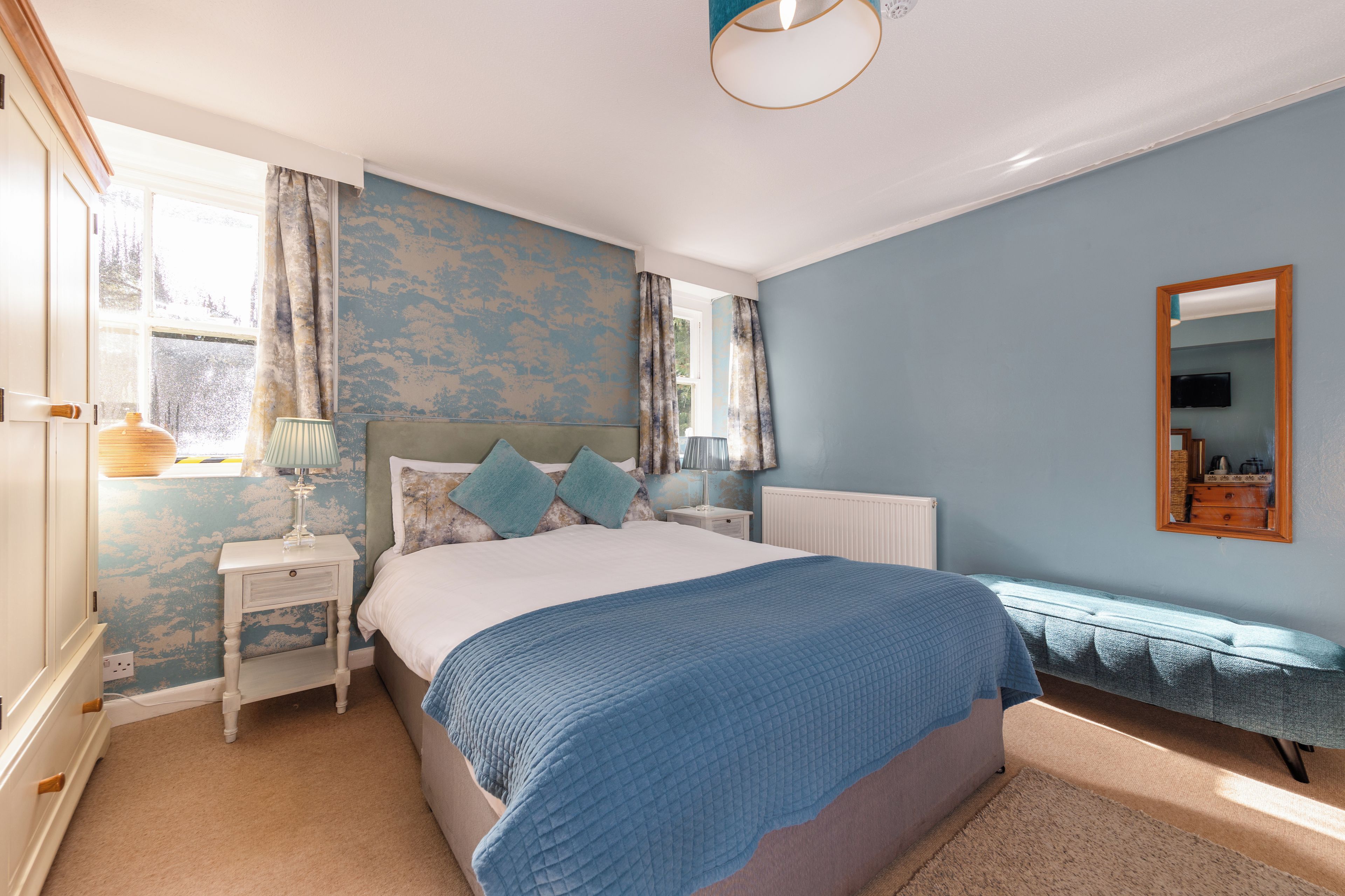 Une chambre à coucher avec un lit, des tables de chevet, une commode, un miroir et une fenêtre avec des rideaux.