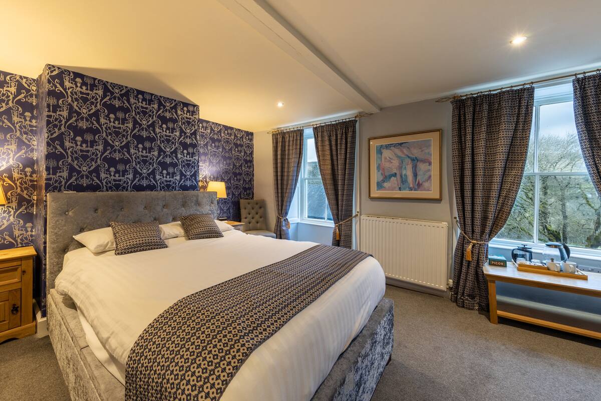 A bedroom with a large bed, two bedside tables with lamps, a radiator, and a window with curtains.