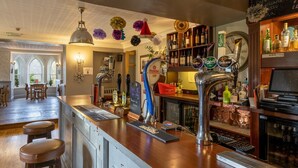 Uma área de bar com balcão de madeira, diversas torneiras e seleção de garrafas.