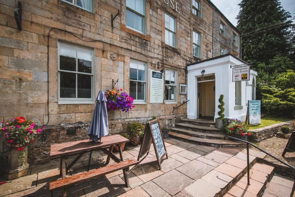 A stone building with a restaurant sign, a bench, and a flower display.