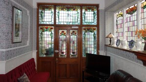 A room with a wooden door with stained glass windows, a red sofa, and a television on a stand. - The Winchester (Great Yarmouth)