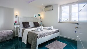 A bedroom with a bed, bedside tables, a window, and an air conditioning unit. - 14 Leoni (Salerno)