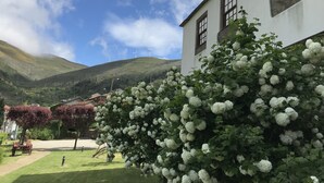 A white building with a garden, a tractor, and wind turbines in the background. - Casa do Monte (Baiao)