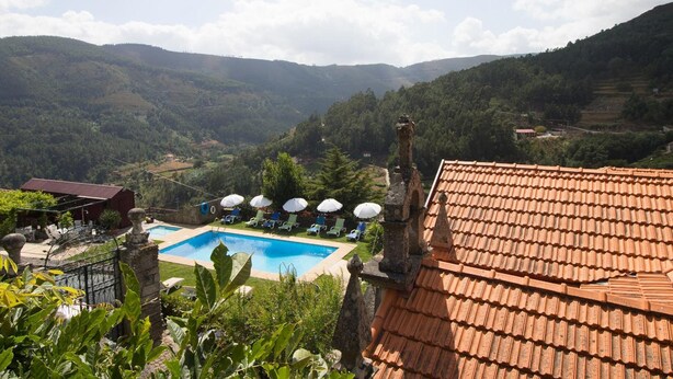 A pool area with a view of the surrounding hills, a red-tiled roof, and a fenced garden. - Casa do Monte (Baiao)