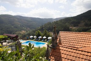 Un espace piscine offrant une vue sur les collines environnantes, un toit recouvert de tuiles rouges et un jardin clos.