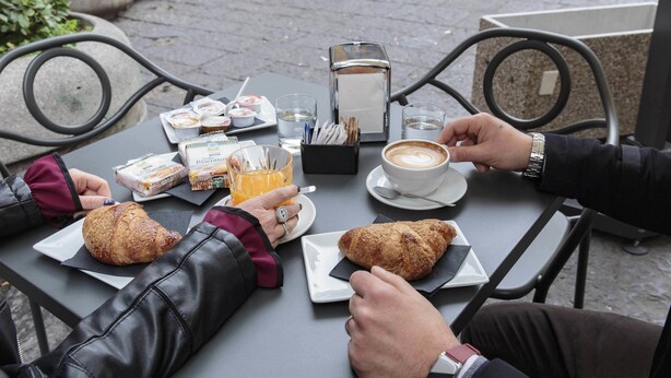 Una mesa con cruasanes, una taza de café y vasos de jugo.