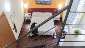 Una habitación de hotel con cama, mesitas de noche, un cuadro en la pared y una escalera.