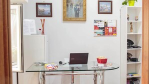 Una habitación con un escritorio de vidrio, una computadora portátil, un tazón rojo, un tablón de anuncios y una estantería.