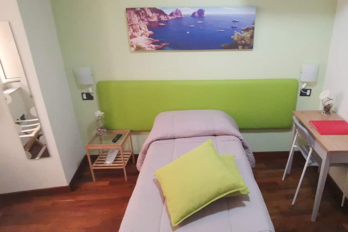 Una habitación con cama, escritorio, silla, mesita y un cuadro en la pared.