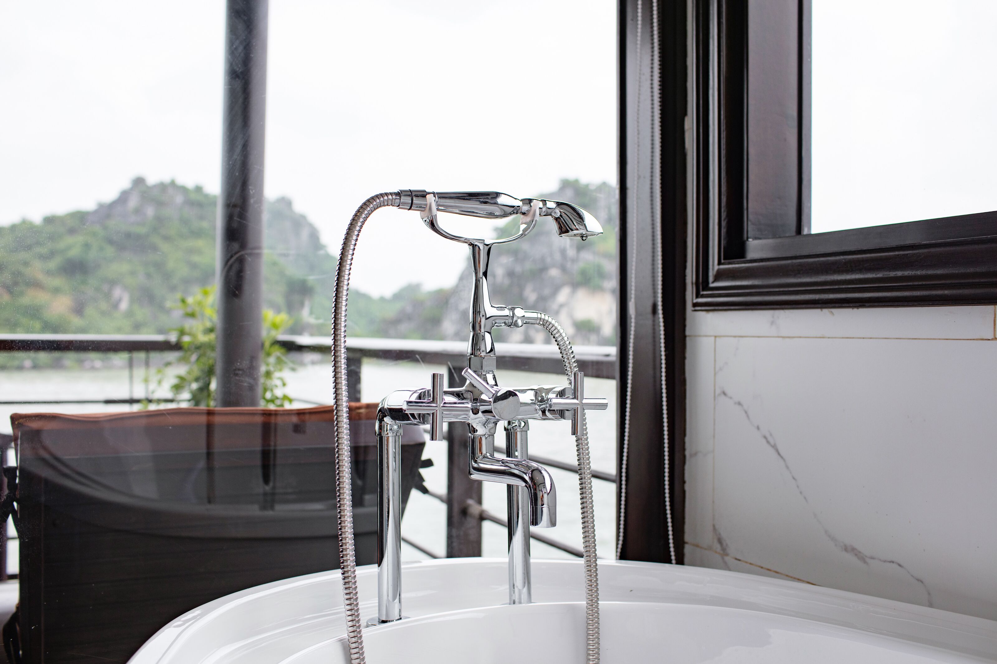 Un baño con un grifo y cabezal de ducha cromados modernos, un lavabo blanco y vistas a un paisaje montañoso a través de una ventana.