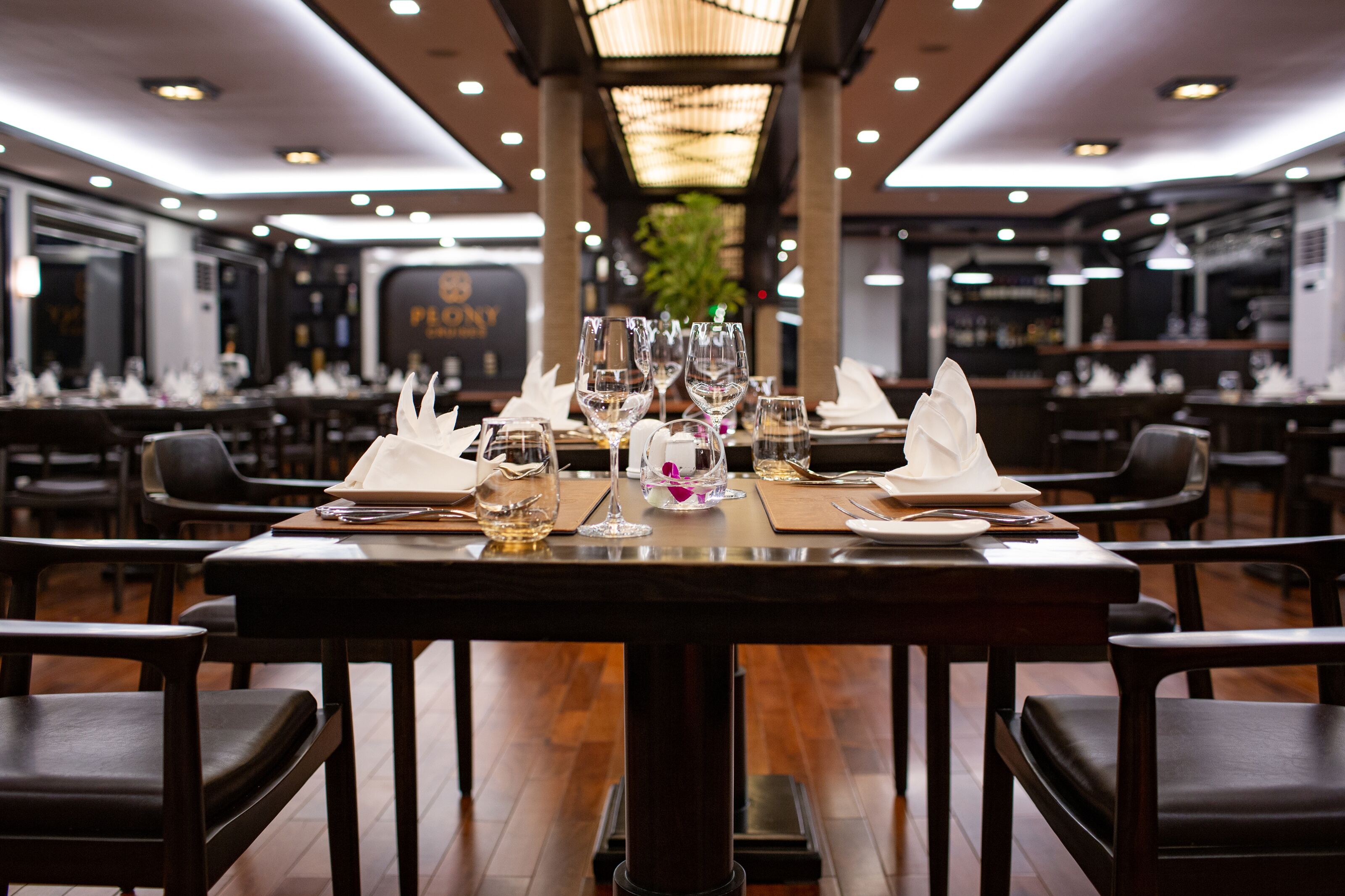 Un restaurante con mesas dispuestas para comer, con servilletas blancas, copas de vino y cubiertos.