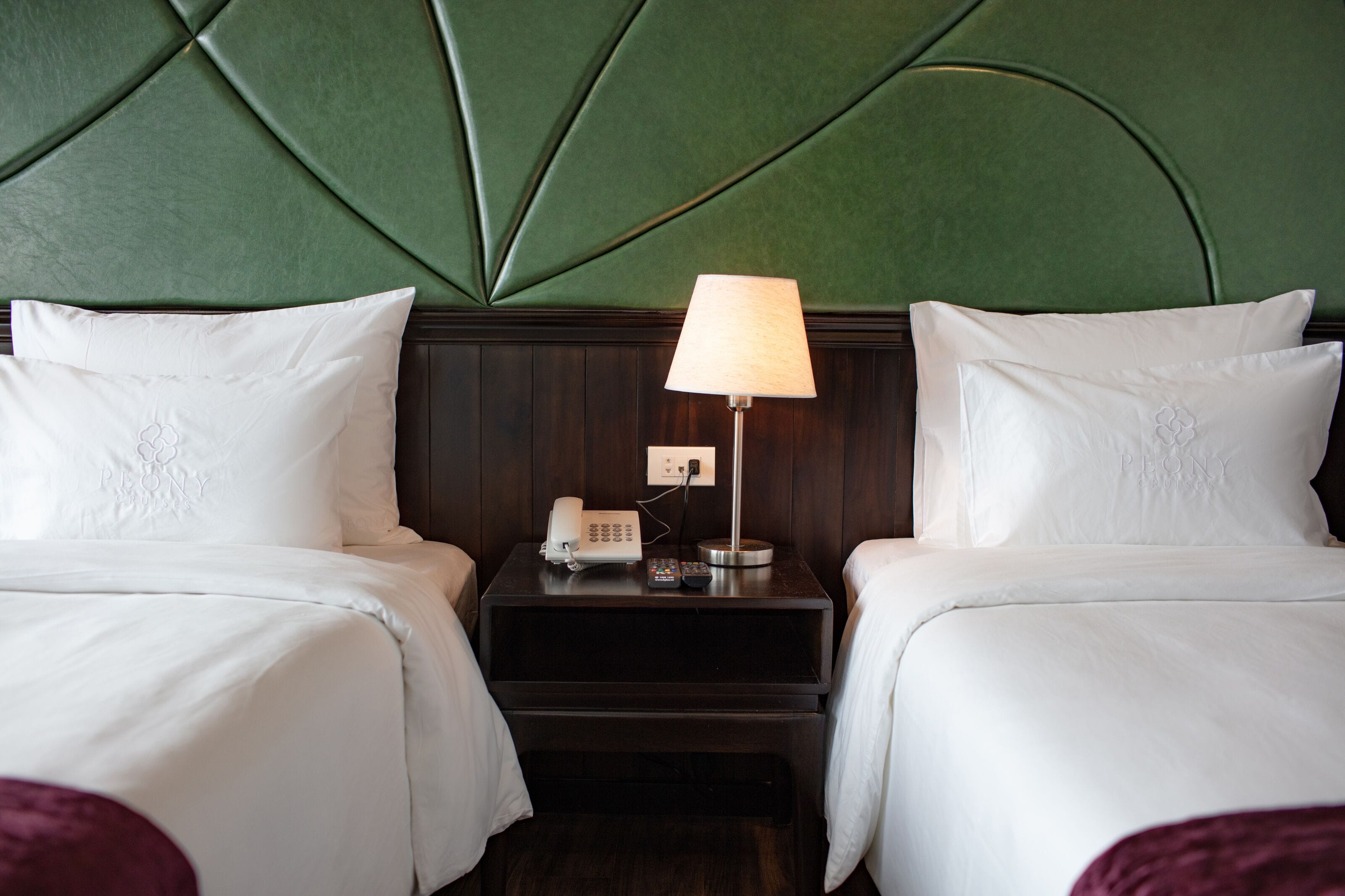 A hotel room with two beds, a nightstand with a lamp, and a wall with a geometric pattern.