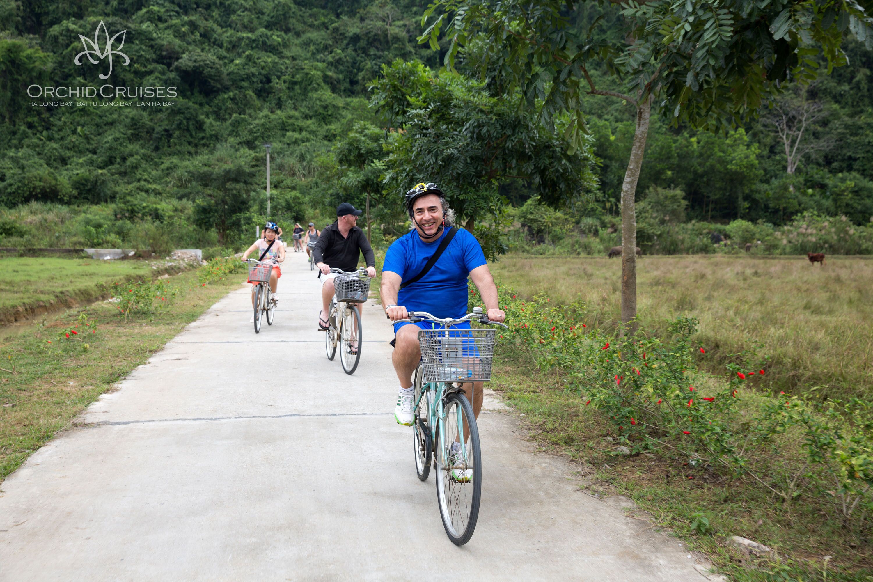 A group of people riding bicycles on a paved path surrounded by greenery.