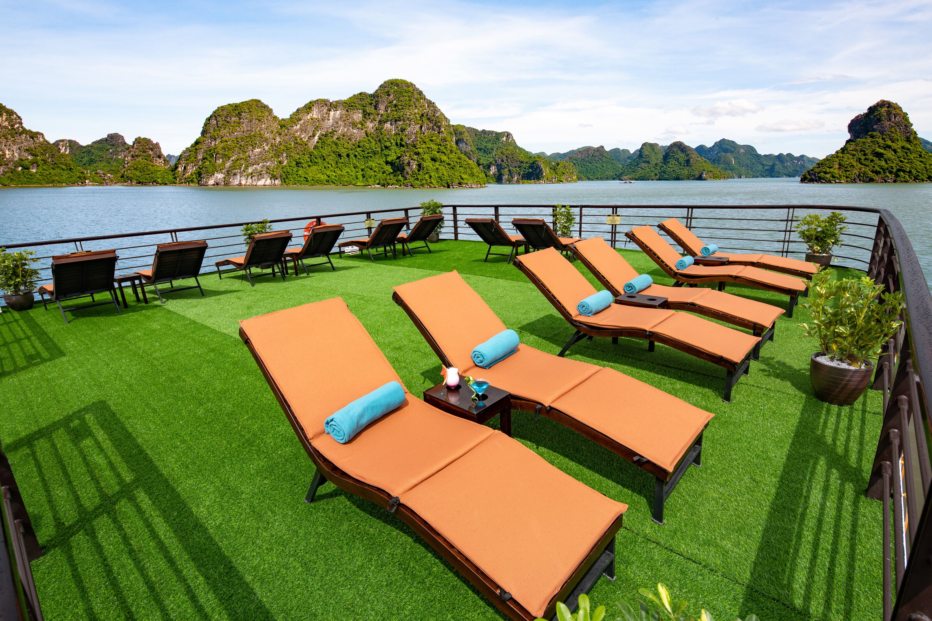 A deck with rows of sun loungers and a view of a lake with mountains in the background.