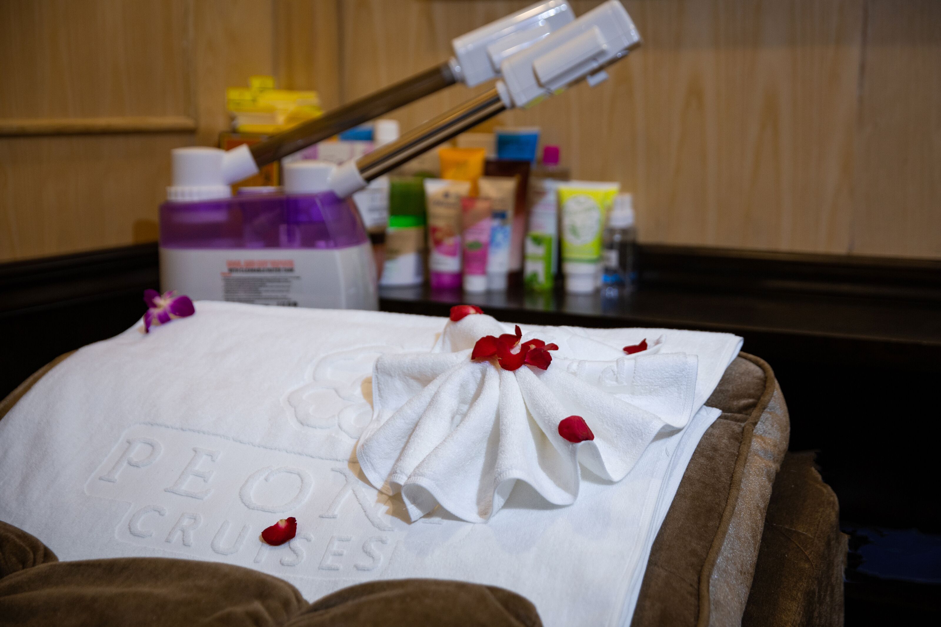 A spa treatment area with a towel on a massage table, a bottle of lotion, and various spa products in the background.