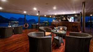 Zona de bar con mobiliario de mimbre y vista al mar al anochecer.