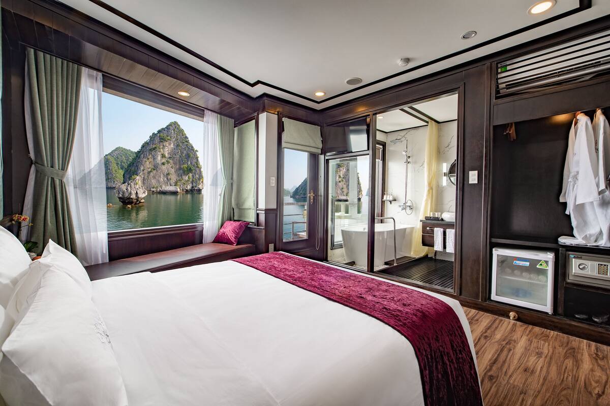 A spacious bedroom with a large bed, a view of a mountainous landscape, a bathroom with a bathtub, and a walk-in closet.