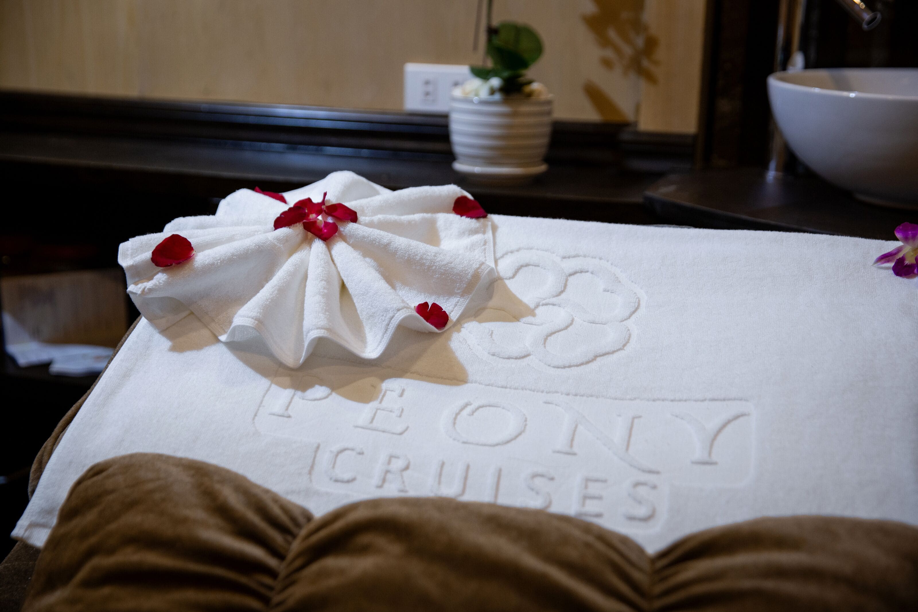 A towel with a floral design and the text "PEONY CRUISES" on a bed.