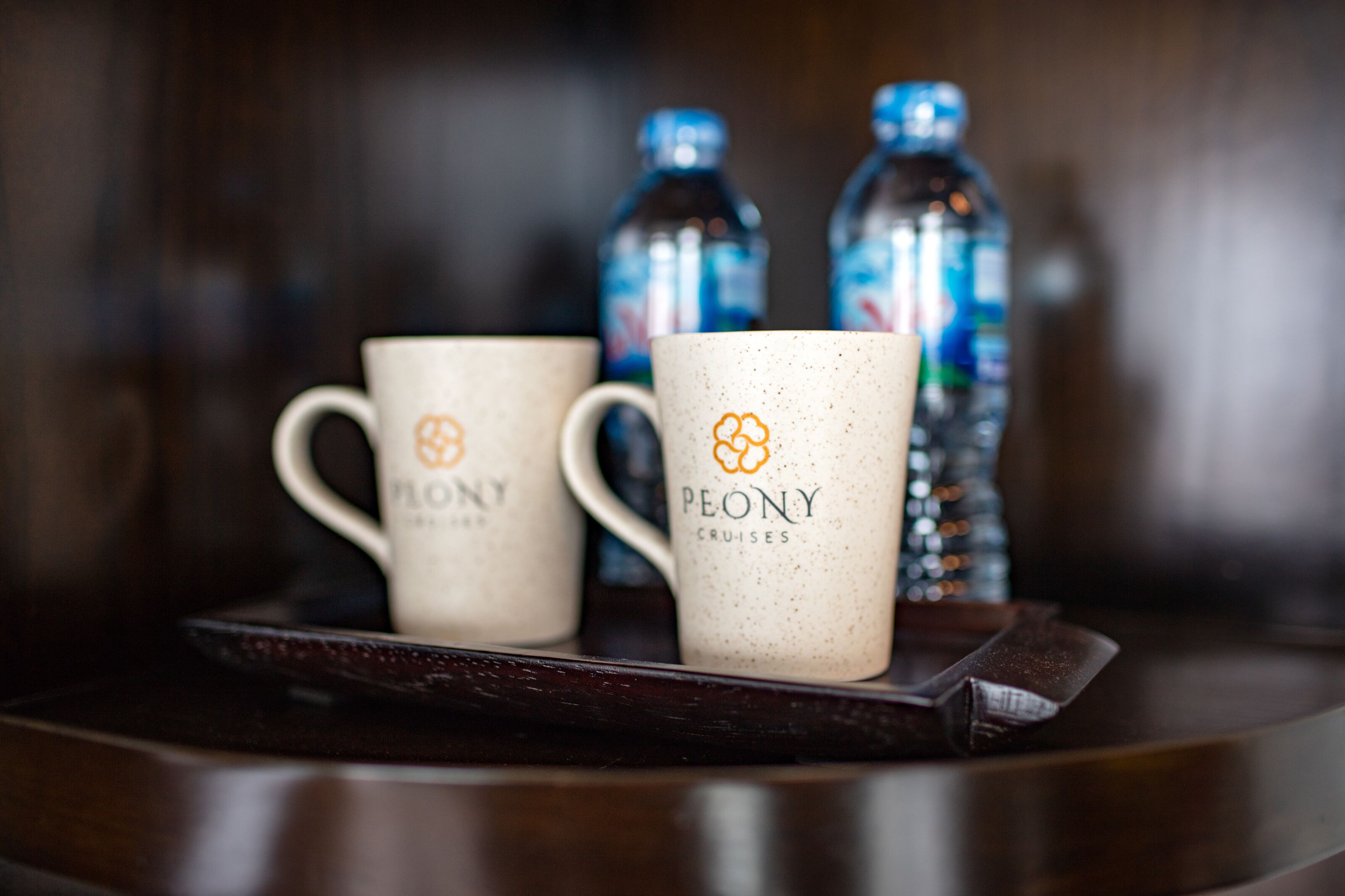 Two Peony Cruises branded mugs on a tray with two water bottles in the background.